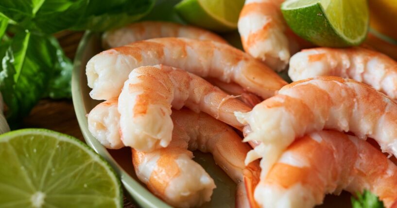 A stock photo of shrimps with lime slices on a wooden table.