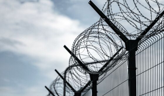 A prison border fence with razor wire against dark sky.
