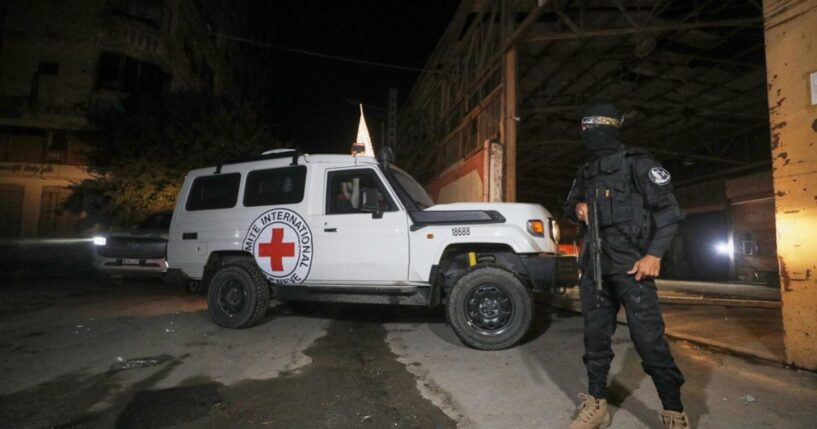 A gunman wearing the uniform of the al-Qassam Brigades, the military wing of Hamas, stands guard as Red Cross vehicles enter a warehouse allegedly to collect coffins containing the bodies of four deceased hostages in Gaza City on Tuesday.