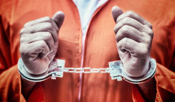 This stock image shows a handcuffed prisoner in an orange jumpsuit.