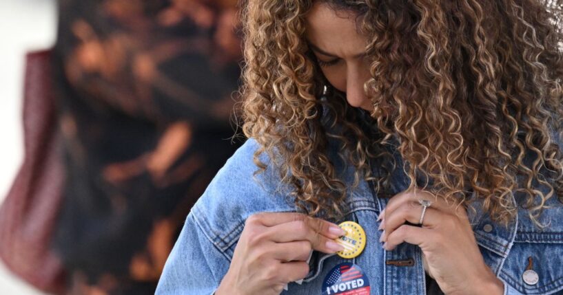 A young woman attaches a pin to her jacket after voting at a mobile outdoor vote center at SoFi Stadium in Los Angeles, California, on Election Day, Nov. 5, 2024.