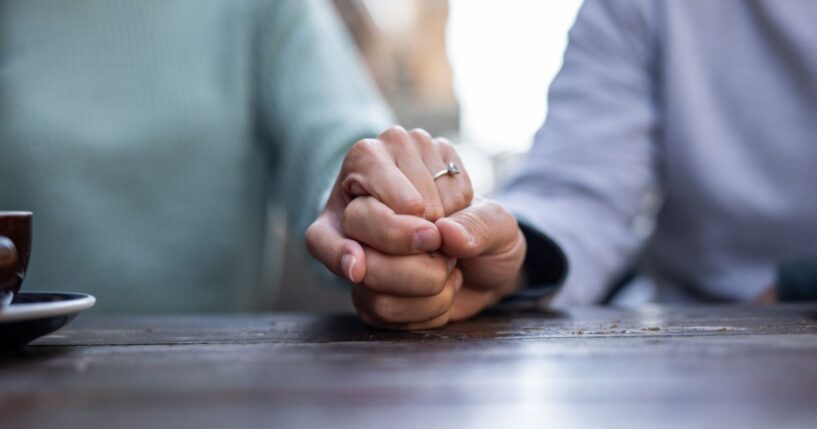 A couple holds hands at a cafe table.