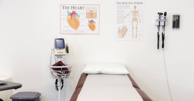 A clean, empty room in a doctor's office with an examination table and various pieces of medical equipment.