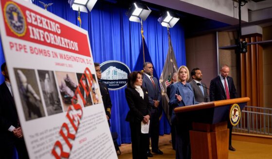 A poster reads "ARRESTED" in bold letters as Attorney General Pam Bondi speaks during a news conference on an arrest of a suspect in the January 6th pipe bomb case at the Department of Justice on Dec. 4, 2025, in Washington, D.C.