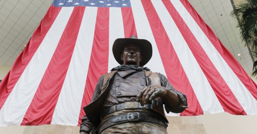 A statue of John Wayne is on display beneath an American flag in John Wayne Airport, located in Orange County, on June 28, 2020, in Santa Ana, California.