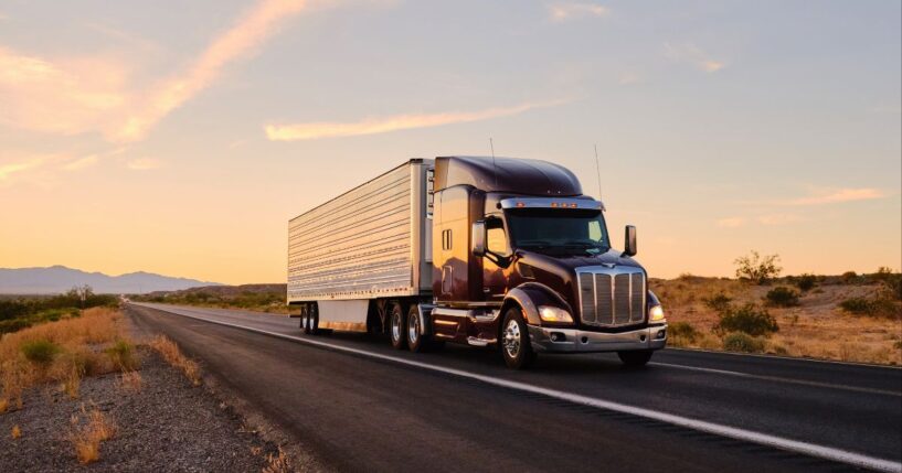A large semi truck hauls freight down an open highway in the Western United States.