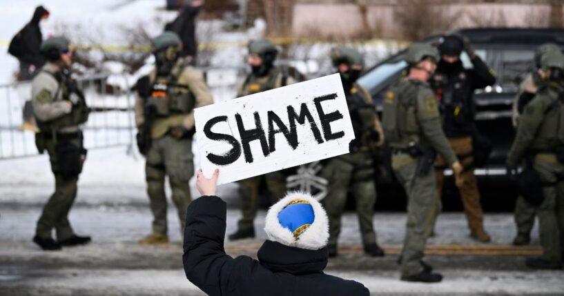 An onlooker holds a sign that reads "Shame" as members of law enforcement work the scene following a suspected shooting by an ICE agent during federal law enforcement operations on Jan. 7, 2026, in Minneapolis, Minnesota.