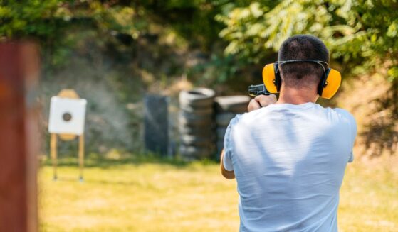 Adult man shooting a target with a handgun in an outdoor shooting range.