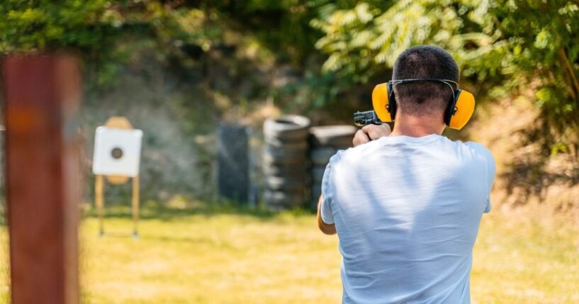 Adult man shooting a target with a handgun in an outdoor shooting range.