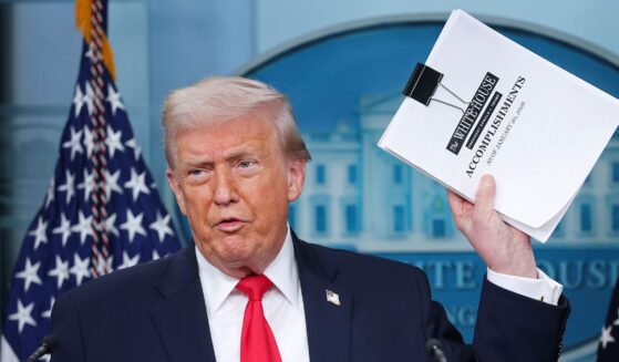 President Donald Trump displays a stack of papers labeled "The White House Accomplishments" as he arrives for a news briefing in the James S. Brady Press Briefing Room of the White House on Jan. 20, 2026, in Washington, D.C.