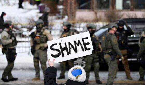 An onlooker holds a sign that reads "Shame" as members of law enforcement work the scene following a suspected shooting by an ICE agent during federal law enforcement operations on Jan. 7, 2026, in Minneapolis, Minnesota.