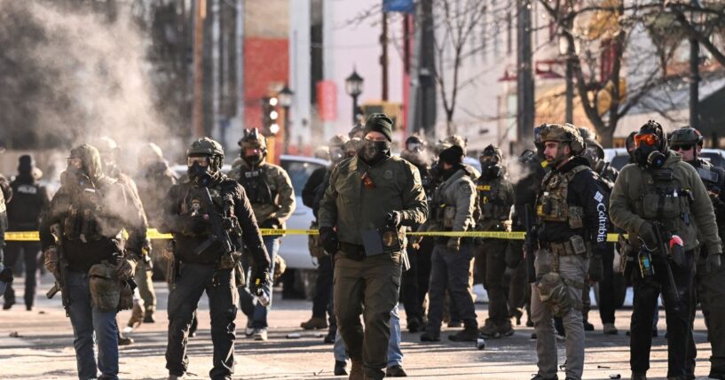 Federal agents stand near police tape as demonstrators gather near the site of where state and local authorities say a man was shot by federal agents earlier in the morning in Minneapolis, Minnesota, on Jan. 24, 2026.