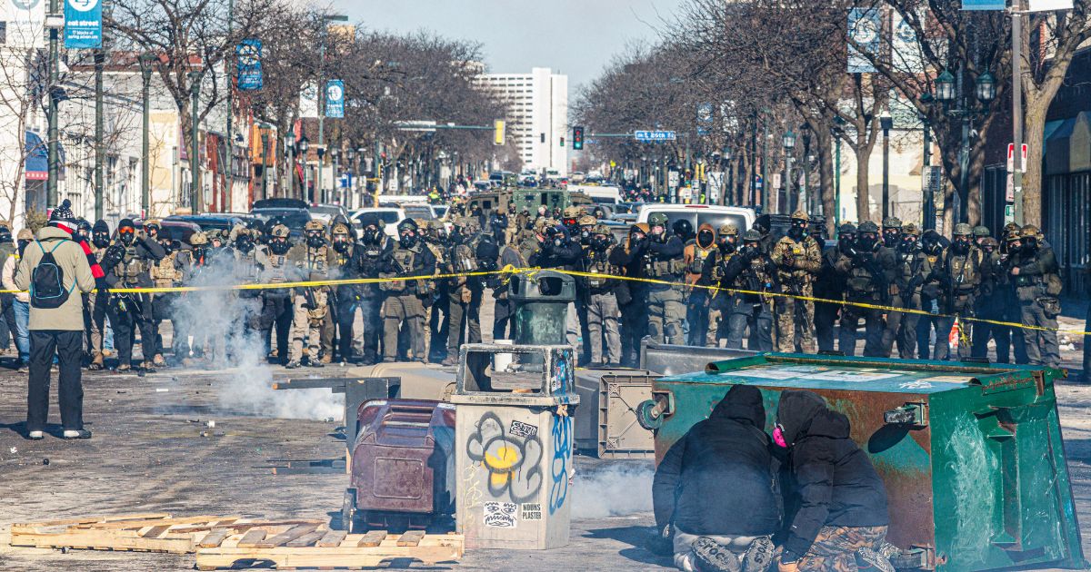 Protesters take cover behind overturned trash containers as a line of federal agents forms a barricade across a downtown street during clashes following the fatal shooting of a demonstrator earlier in the day, on Jan. 24, 2026, in Minneapolis, Minnesota.