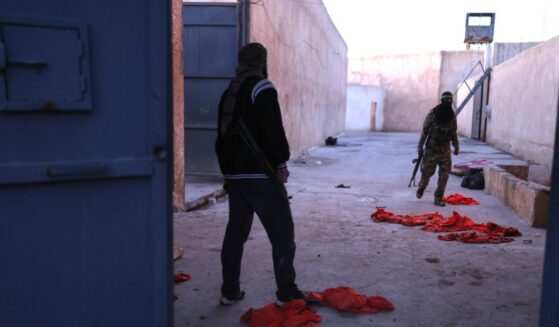 Syrian government fighters walk inside Al-Shaddadi prison, where red detainee suits lie on the ground, in the town of Shaddadeh, northeastern Syria, on Tuesday, a day after Syria's Interior Ministry said Islamic State group members escaped from the facility during clashes with the Kurdish-led Syrian Democratic Forces.