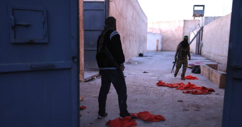 Syrian government fighters walk inside Al-Shaddadi prison, where red detainee suits lie on the ground, in the town of Shaddadeh, northeastern Syria, on Tuesday, a day after Syria's Interior Ministry said Islamic State group members escaped from the facility during clashes with the Kurdish-led Syrian Democratic Forces.
