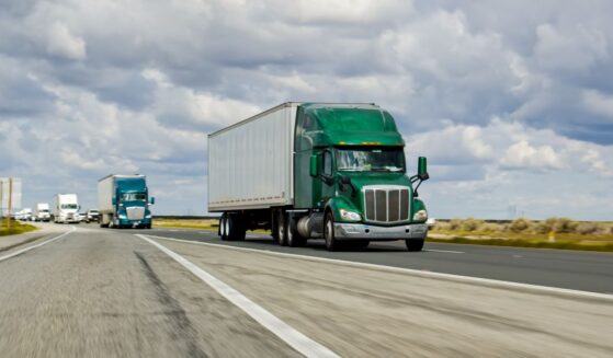 A green truck driving on Interstate 5 in California on an overcast day.