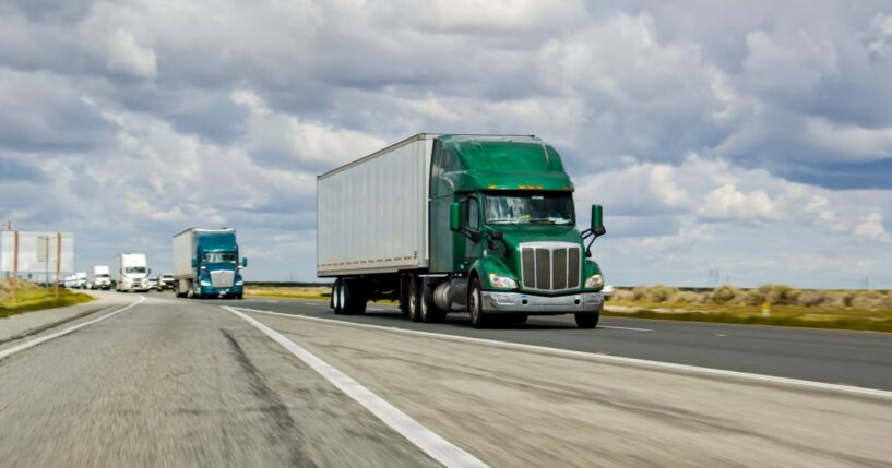 A green truck driving on Interstate 5 in California on an overcast day.