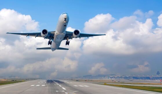 An airplane takes off from a runway under a blue sky.
