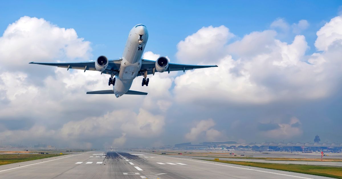 An airplane takes off from a runway under a blue sky.