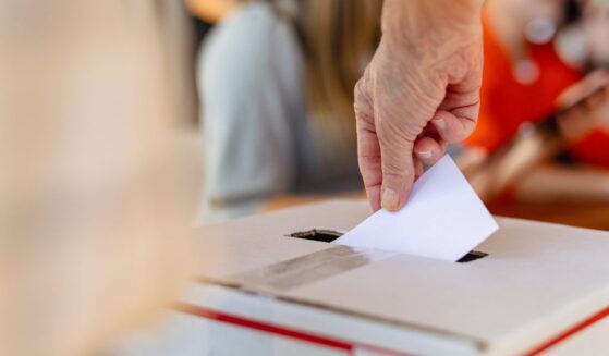 A close-up picture of a hand placing a ballot in a ballot box.