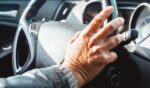 A senior adult holds the steering wheel to a car.