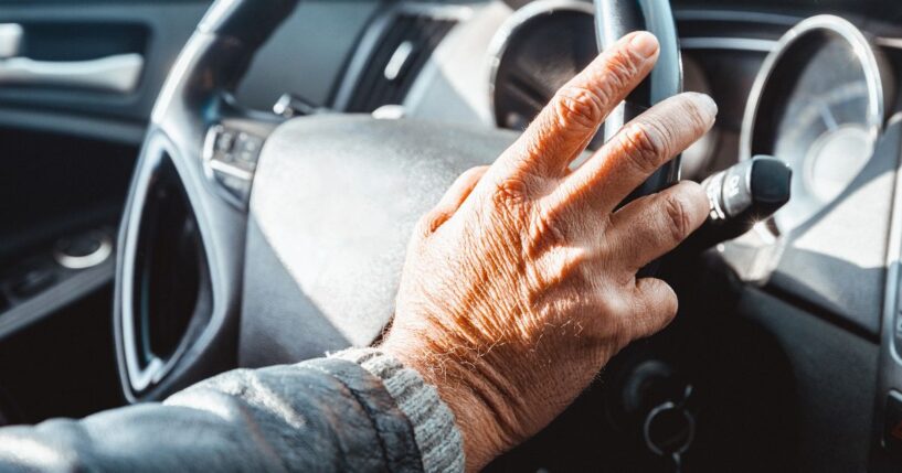 A senior adult holds the steering wheel to a car.