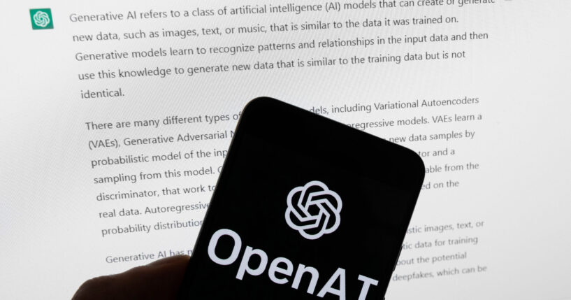 The OpenAI logo is displayed on a mobile phone in front of a computer screen with output from ChatGPT on March 21, 2023, in Boston, Massachusetts.
