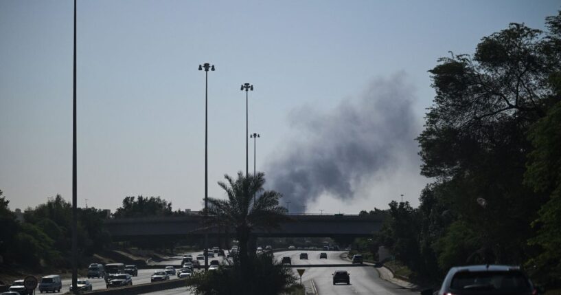 Motorists drive along a street as smoke rises from a reported Iranian strike in the area where the U.S. Embassy is located in Kuwait City on March 2, 2026.