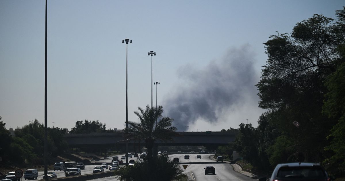 Motorists drive along a street as smoke rises from a reported Iranian strike in the area where the U.S. Embassy is located in Kuwait City on March 2, 2026.