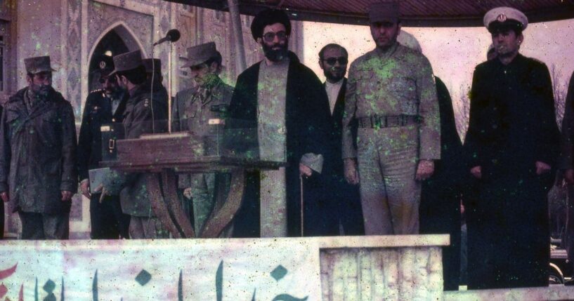 Iranian President Ali Khamenei surrounded by soldiers on stage in March of 1983.