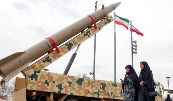 A ballistic missile launch vehicle sits as two women walk past in Tehran on Feb. 11, 2026.
