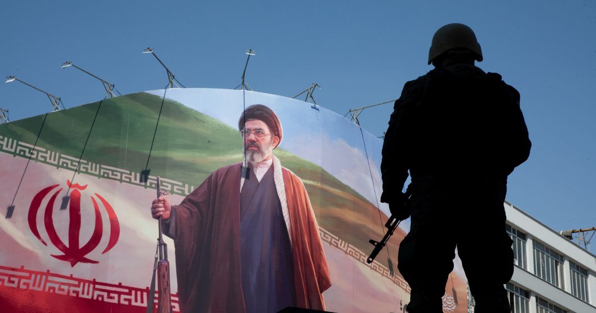 A member of the Iranian security forces stands guard under a large portrait of Iran's new Supreme Leader, Mojtaba Khamenei, during a memorial to mark the 40th day since his father, Ali Khamenei, was killed in U.S.-Israeli joint strikes on April 9, 2026, in Tehran, Iran.