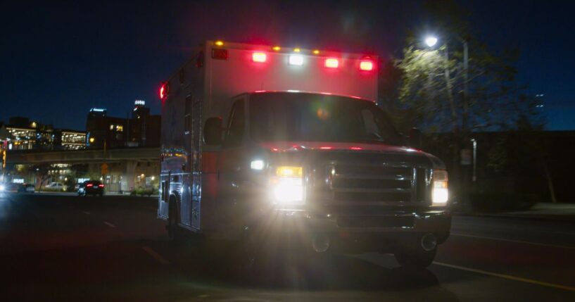 An ambulance driving through a downtown district at night.
