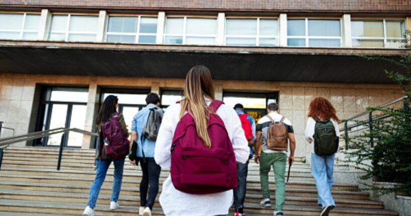 Students walk up the steps of a schoolhouse.