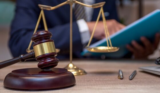 A person sits at a desk analyzing files as the weights of Justice stand and a gavel sits.