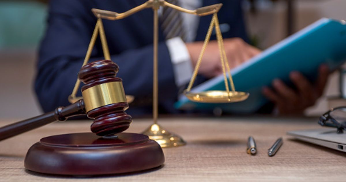 A person sits at a desk analyzing files as the weights of Justice stand and a gavel sits.