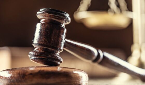 A gavel lays on a wooden block next to a balancing scale in a dark room.