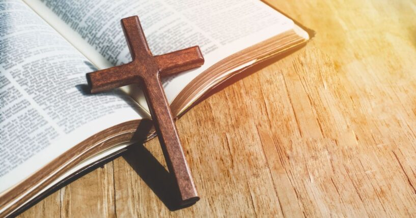 A close up of a small cross leaning against an open Bible.