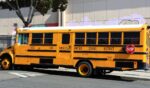 A Los Angeles Unified School District yellow school bus drives down the street in the daylight.