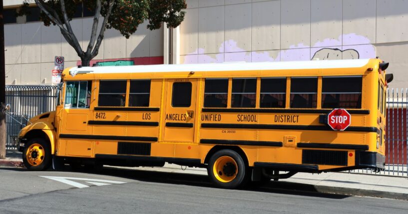 A Los Angeles Unified School District yellow school bus drives down the street in the daylight.