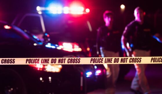Two police officers walk in front of flashing patrol cars at a crime scene.