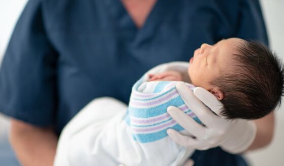 A nurse holds a newborn baby at a hospital as the child sleeps.