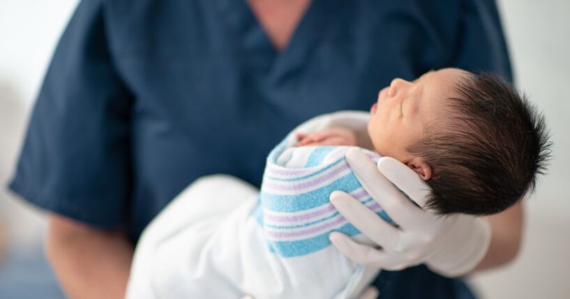 A nurse holds a newborn baby at a hospital as the child sleeps.