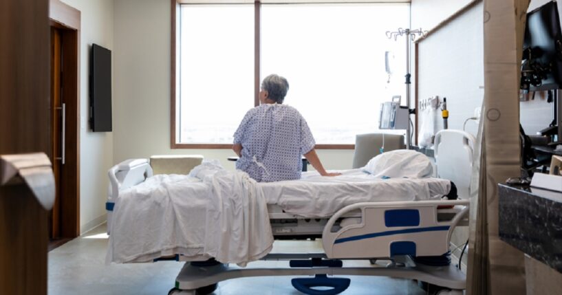 A photo illustration depicts an older woman seated on a hospital bed alone in her room.