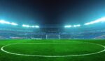 An illuminated soccer stadium at night with a green field and empty stands, ready for an exciting match under bright blue floodlights.