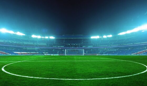 An illuminated soccer stadium at night with a green field and empty stands, ready for an exciting match under bright blue floodlights.