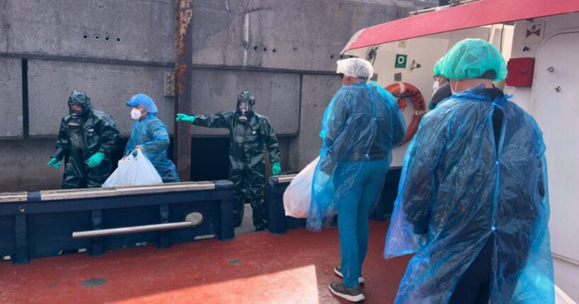 Passengers dressed in masks, plastic suits, and head coverings are escorted off the hantavirus-stricken cruise ship MV Hondius Sunday at the port of Granadilla in Tenerife, Canary Islands, Spain.