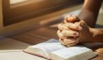 Hands on the Bible in a prayerful position.