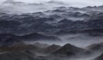 Mountains stand in swaths of fog.