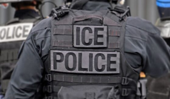 An ICE officer in his uniform stands among his colleagues.